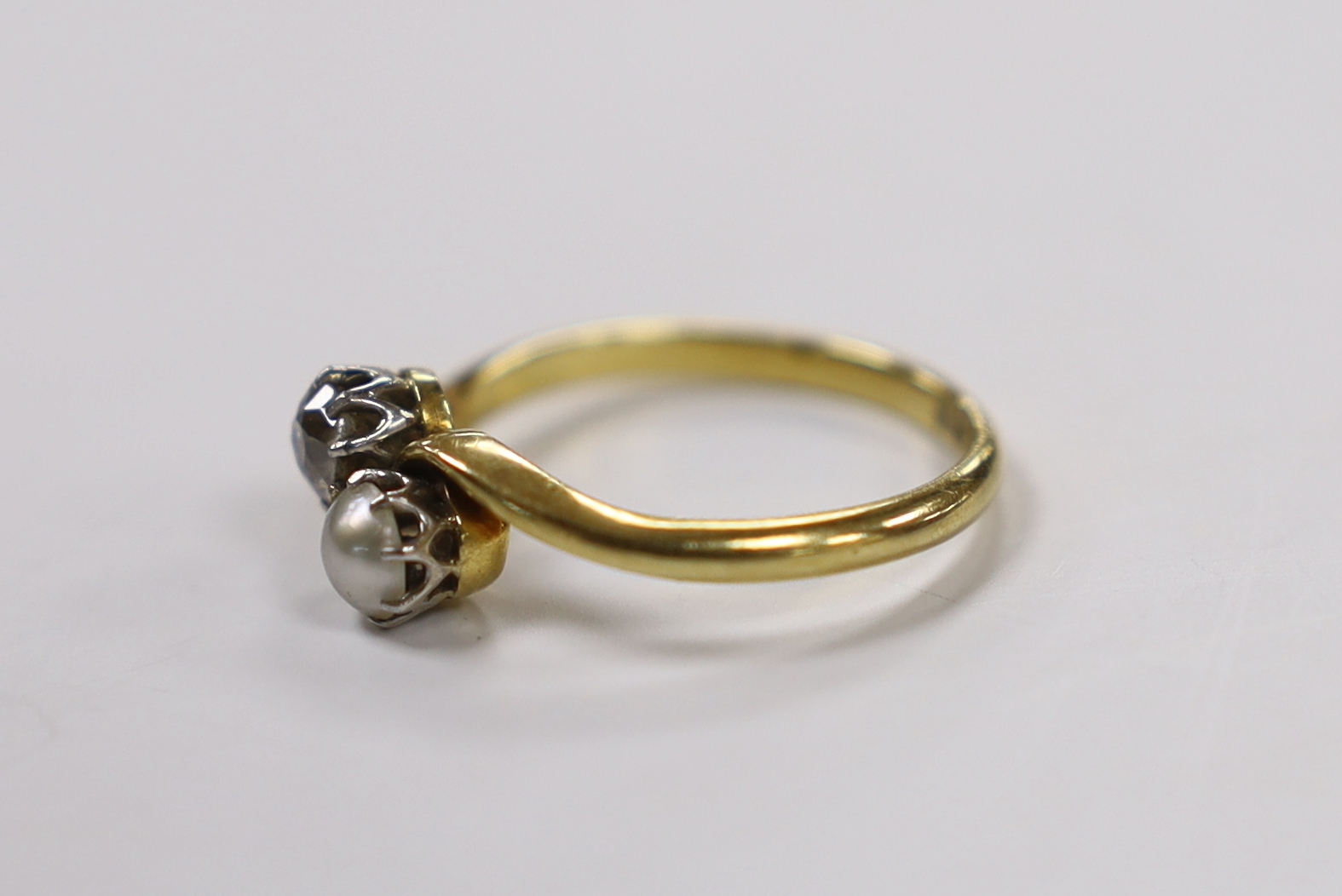 An 18ct, single stone diamond and single stone cultured pearl set crossover ring, size L/M, gross weight 2.6 grams.